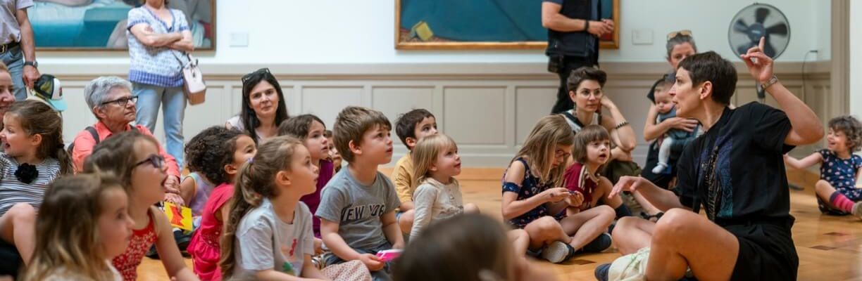 Jeune public assis par terre écoutant une médiatrice du MAH