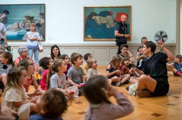 Jeune public assis par terre écoutant une médiatrice du MAH