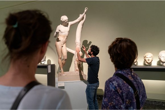 guide présente une sculpture antique devant deux visiteuses au Musée d'art et d'histoire