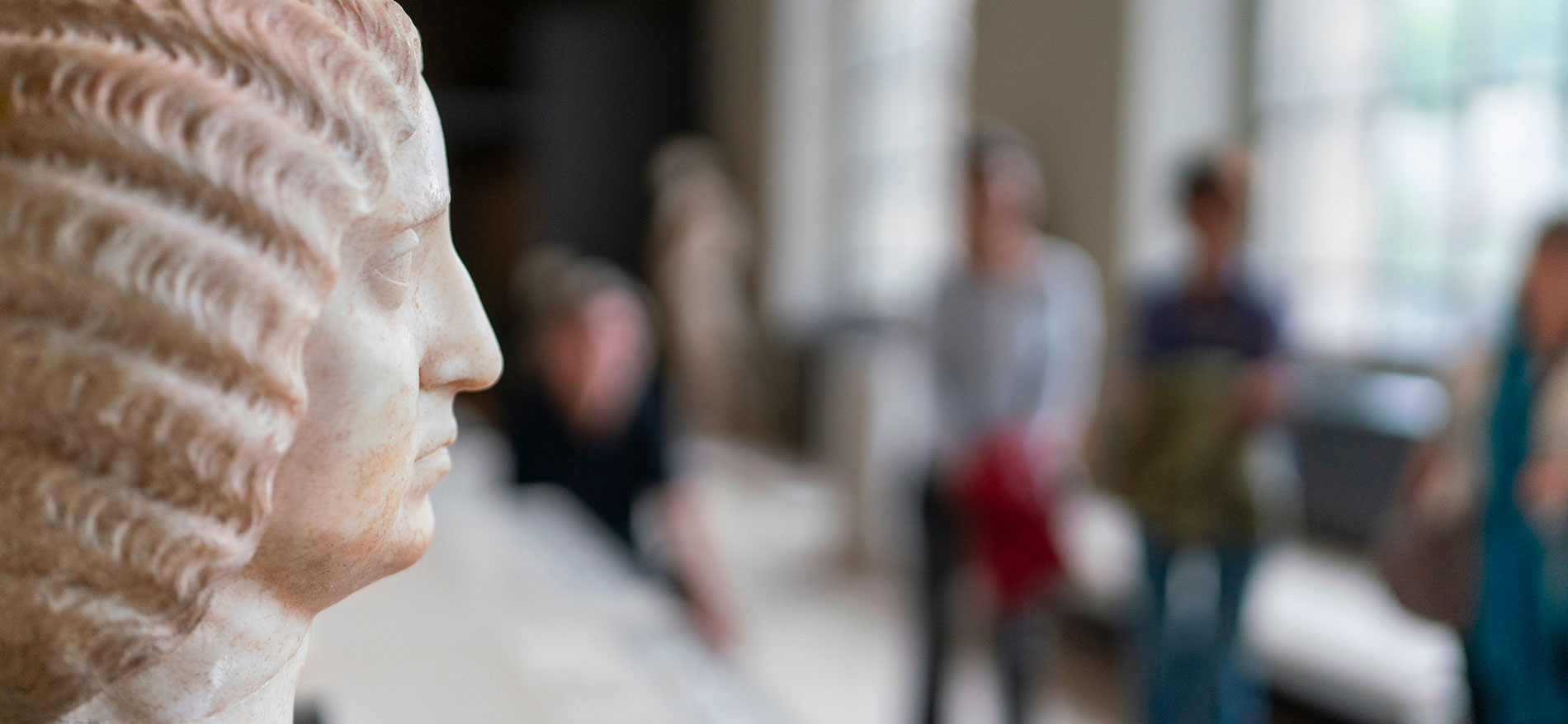 profil d'une statue au premier plan avec visiteurs et visiteuses au second plan flou