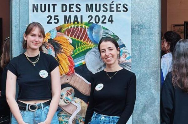 deux personnes souriantes devant l'affiche de la nuit des musées 2024 devant le mamco entourée d'autres visiteurs