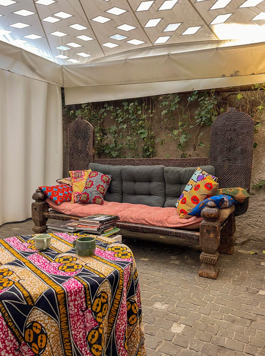 Cour intérieure du Musée Barbier-Mueller avec un sofa en bois recouvert de coussins colorés et une table avec un tisse en wax