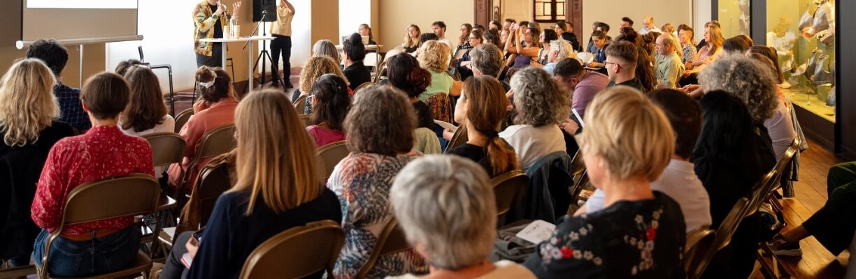 Soixantaine de personnes assises pour écouter un orateur dans la salle des armures du MAH