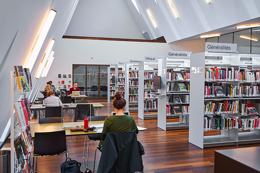 Bibliothèque du MEG : 6 rayonnages et personnes assises aux table