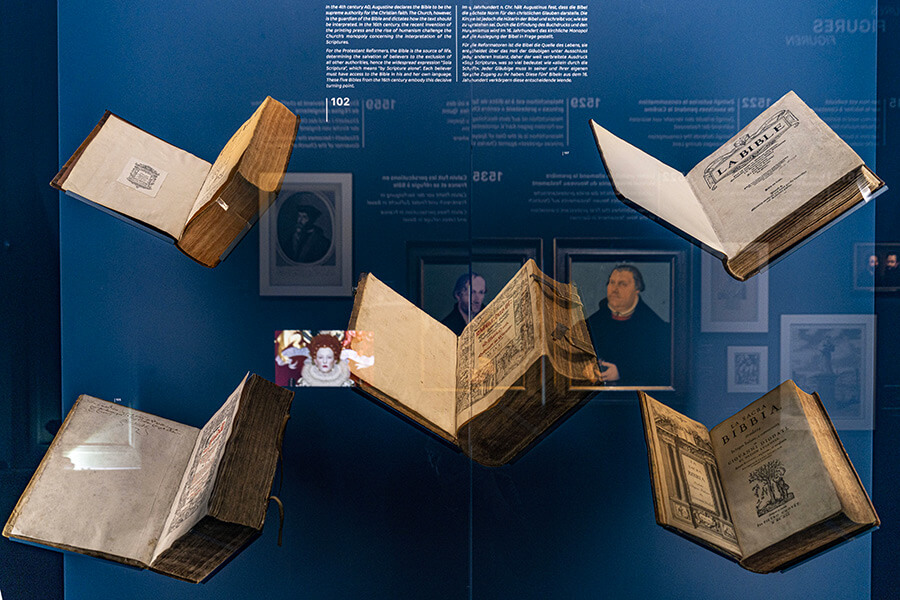 Vitrine d'exposition avec 5 livres ouverts donnant l'impression qu'ils volent, deux livres sont des bibles, Musée de la Réforme