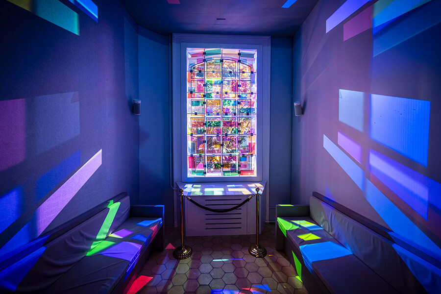 Vitrail moderne dont les couleurs bleues, vertes, rouges et mauves se reflètent sur les murs et le sol du Musée de la Réforme