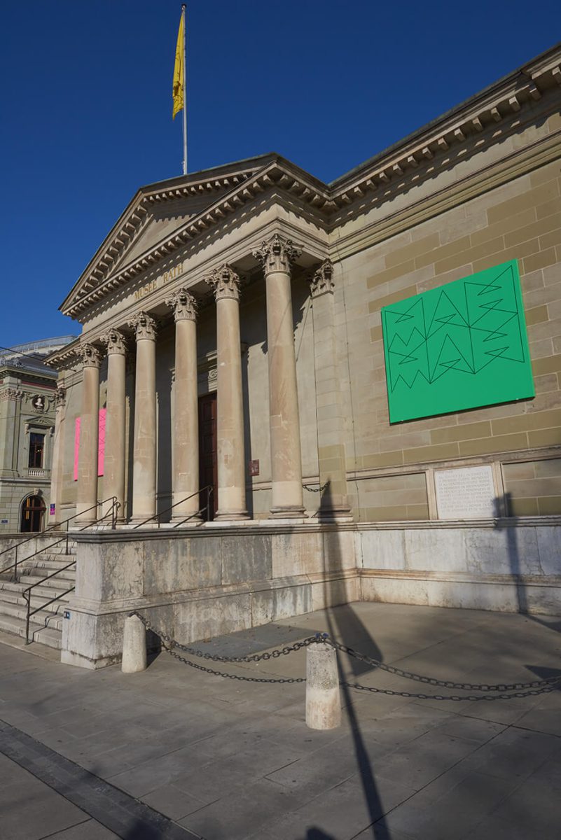 Façade du MAH prise de côté, ciel bleu et drapeau jaune