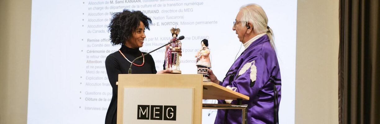 Carine Durant échangeant une poupée avec un homme âgé aux cheveux longs et blancs au MEG