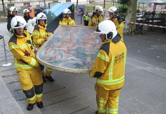 six pompiers en tenue jaune et casque blanc en train de porter une peinture de grand format