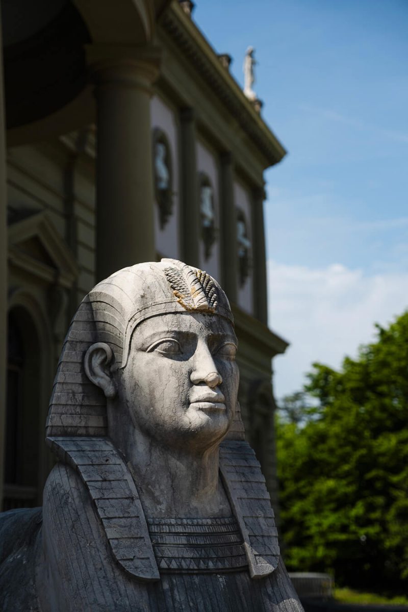 Statue de sphynx au premier plan devant la façade du Musée Ariana