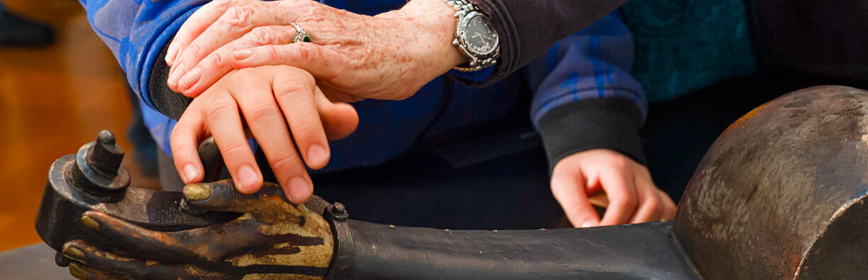 Zoom sur une main âgée sur une main plus jeune qui touche une sculpture