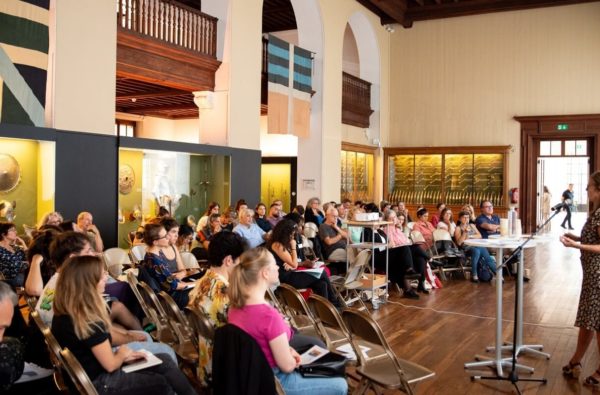 Public assis dans la salle des armures du MAH écoutant une oratrice