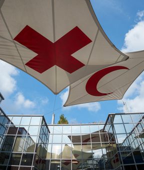 Drapeaux de la Croix-Rouge et du Croissant-Rouge dans l'enceinte du MICR. Ciel bleu